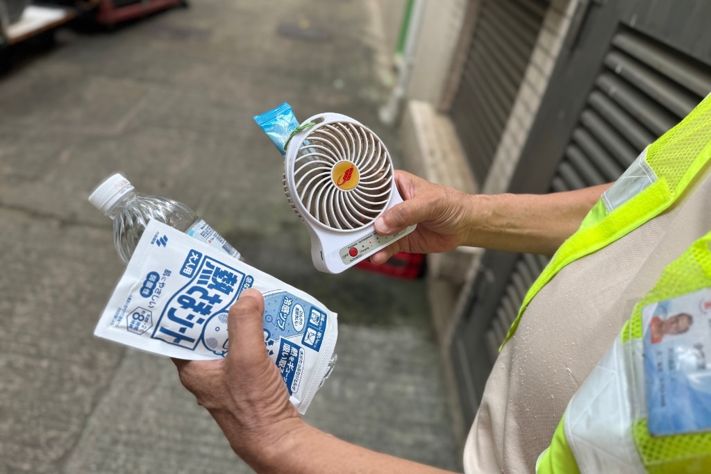 A cleaner in Tsuen Wan, Hong Kong, seeks shade in a back alley with a portable fan on July 4, 2025.
